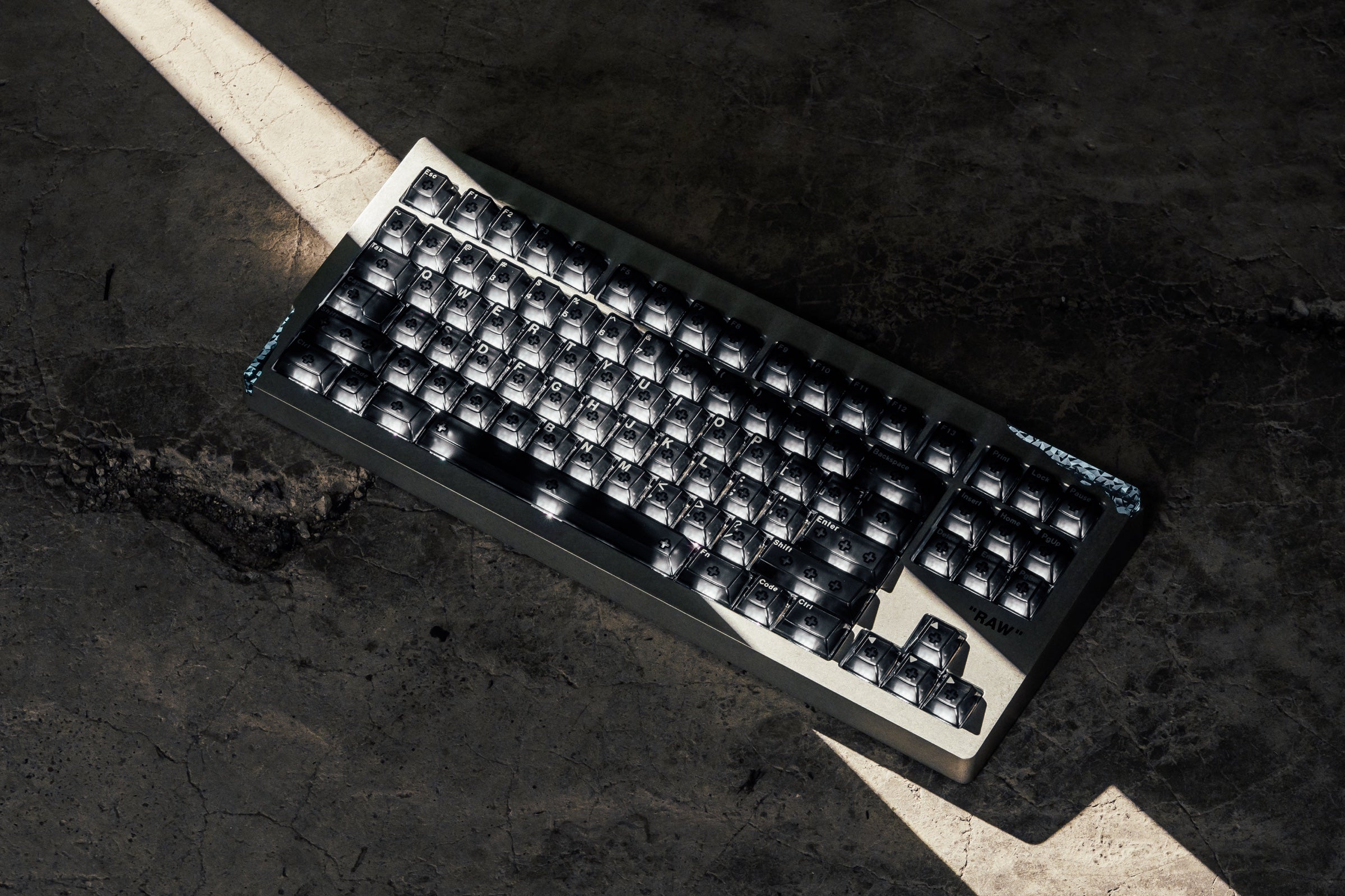 Angry Miao AM Relic 80 RAW keyboard seen from above on dark concrete, crossed by a narrow beam of light.