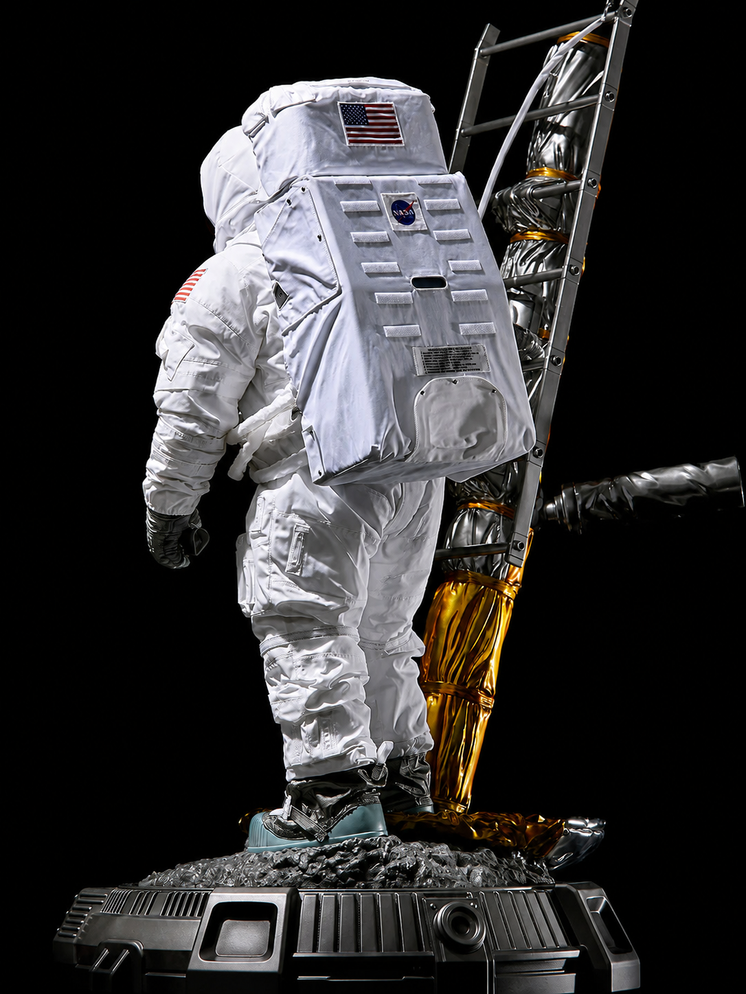 Rear view of the astronaut sculpture showing the fabric PLSS, ladder, lunar ground, and base.