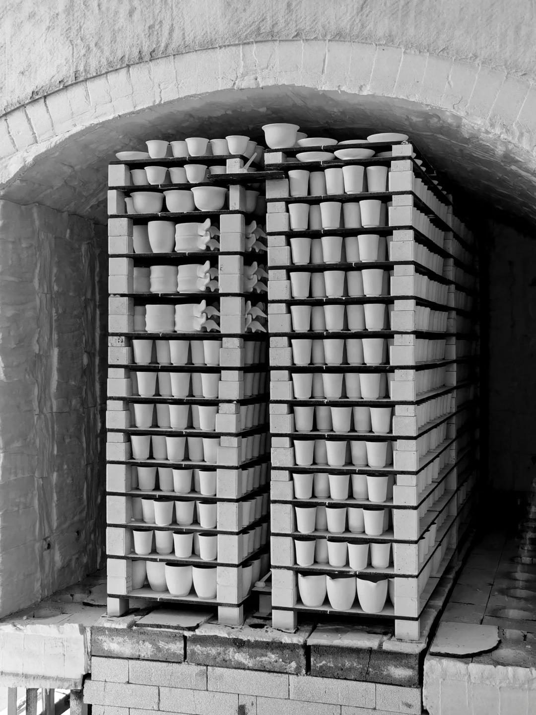 Porcelain vessels stacked on shelves inside a kiln