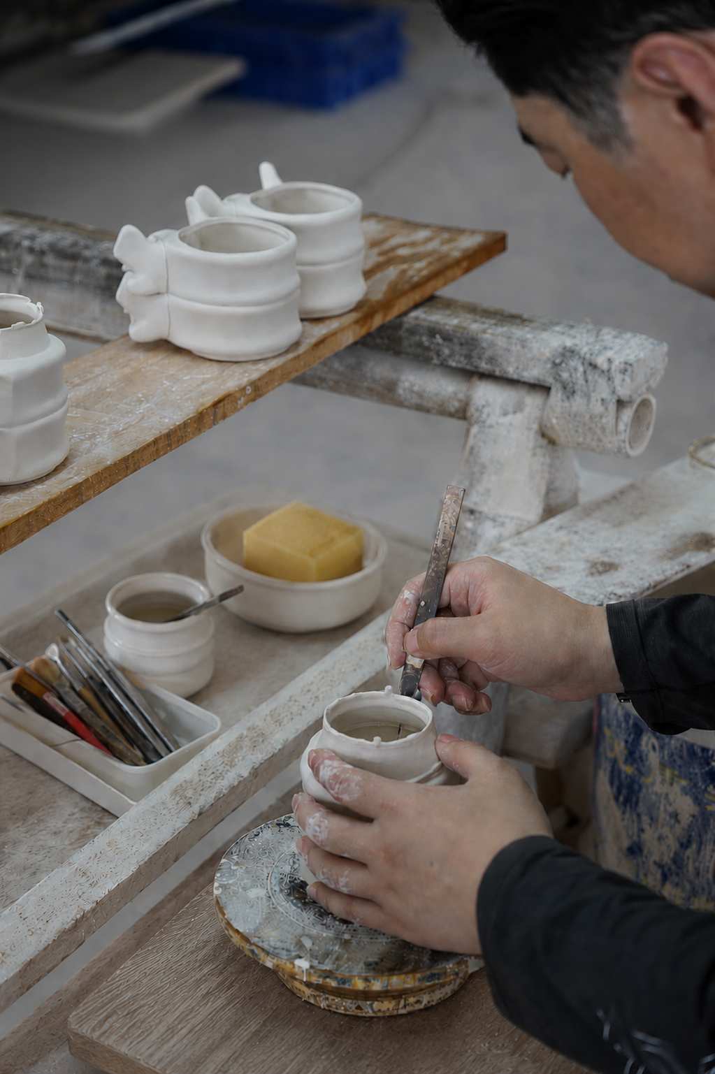 Craftsperson trimming excess porcelain from a freshly molded cup body